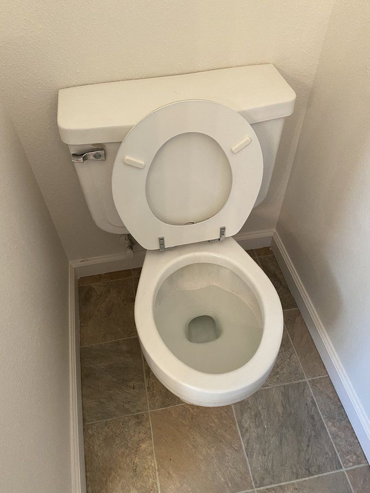 White toilet with the seat up in a small bathroom with tile flooring.