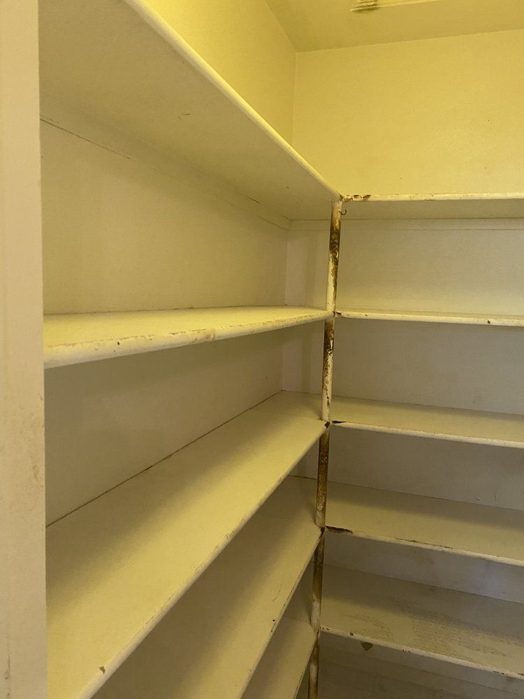 Empty white shelves in a corner pantry, with visible wear and tear.