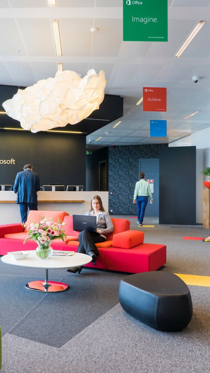 Modern office lobby with red and orange seating, woman using a laptop, and 