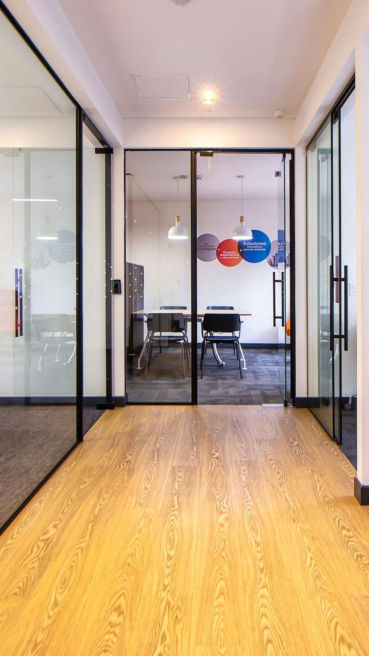 Hallway with glass-walled rooms, wood floor, and meeting room in the distance, featuring colorful circular decals.