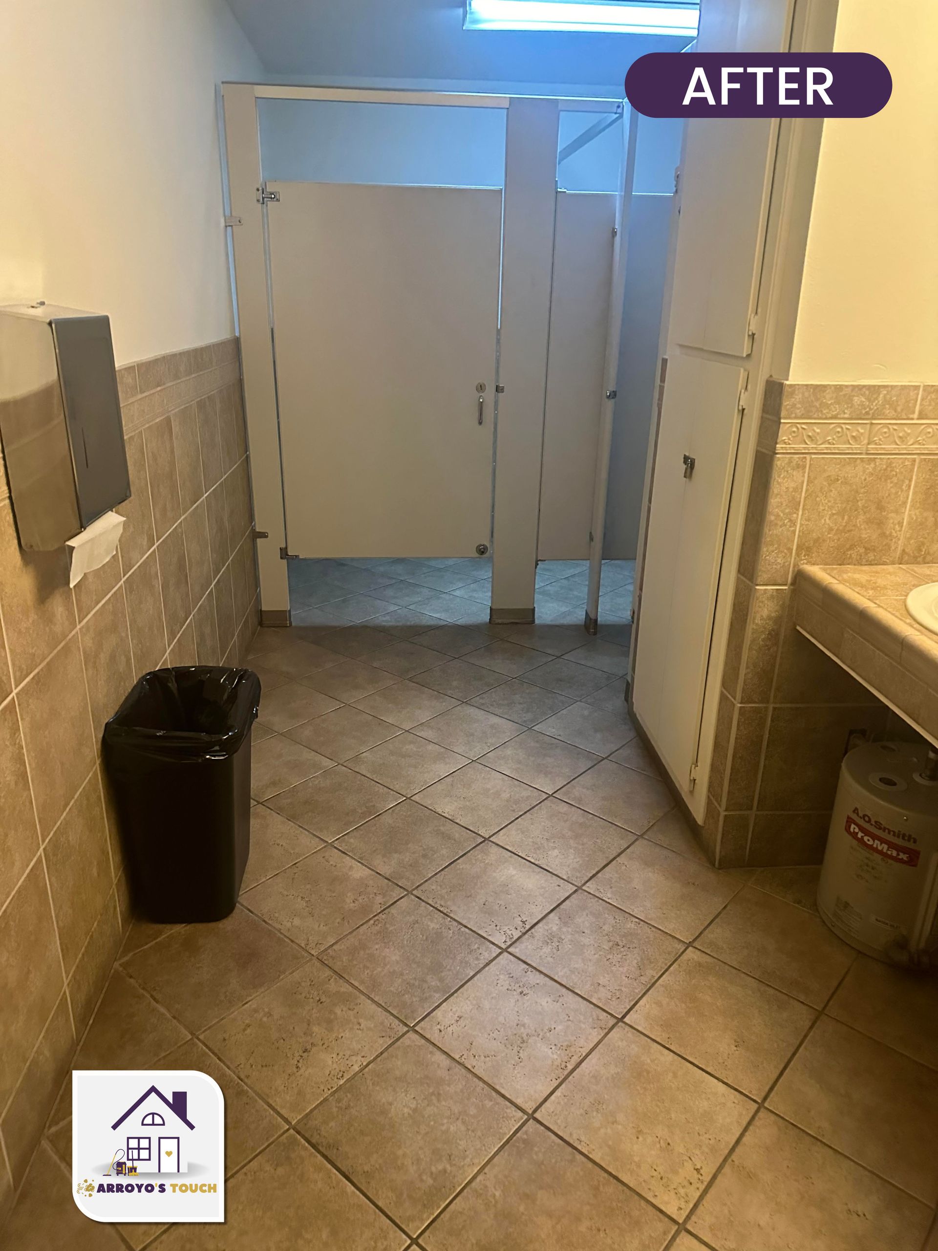A renovated public restroom featuring tan tiled floor and walls, white stall doors, and a black trash can.