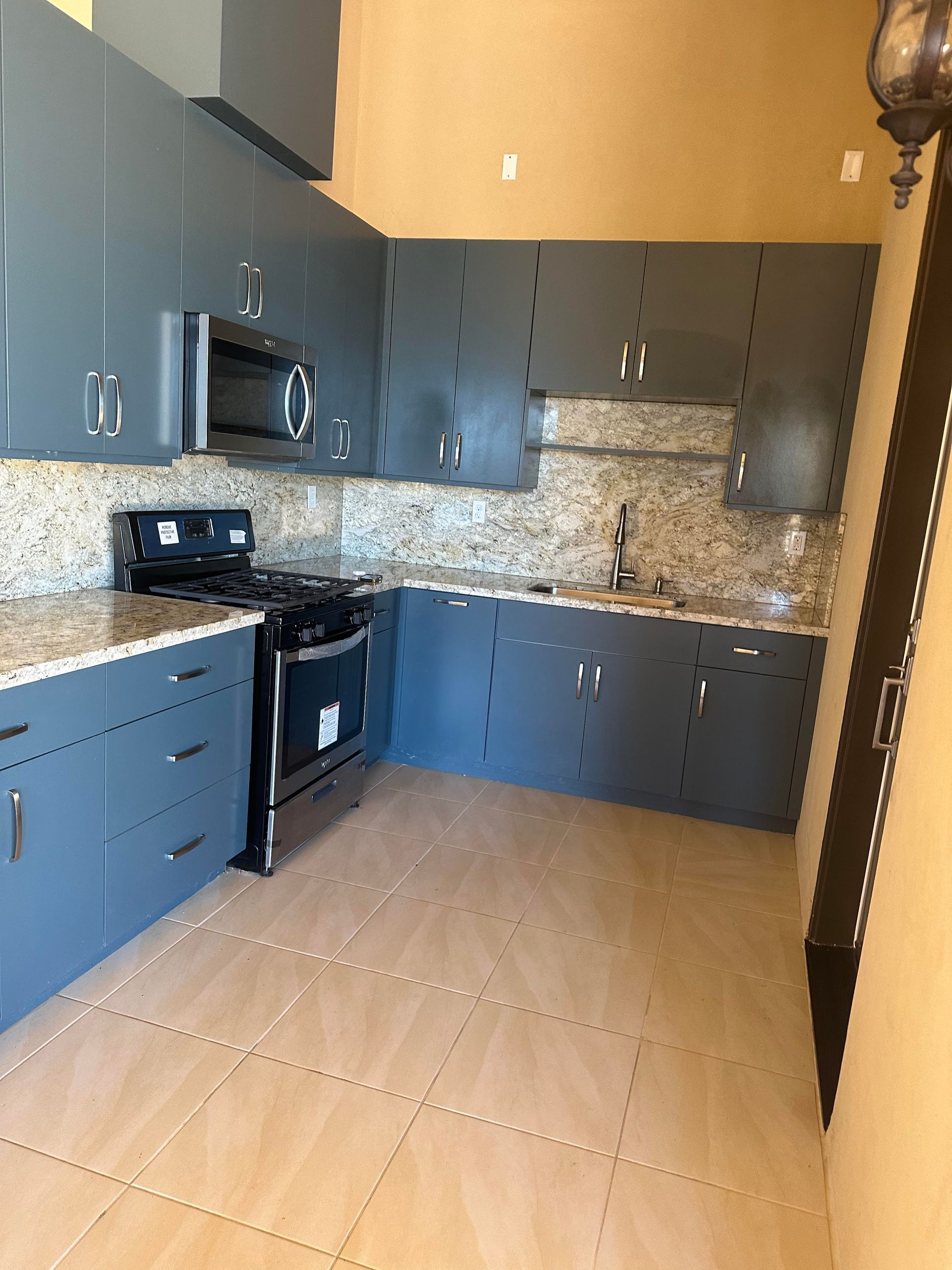 Blue kitchen cabinets, stainless steel appliances, beige countertops and tile floor.