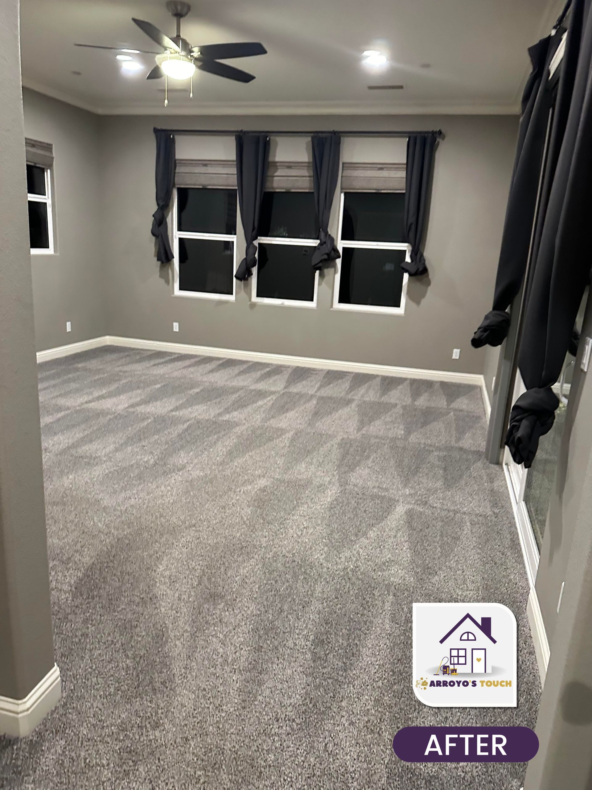 Gray carpeted room with gray walls, three windows with dark blue curtains, and a ceiling fan.