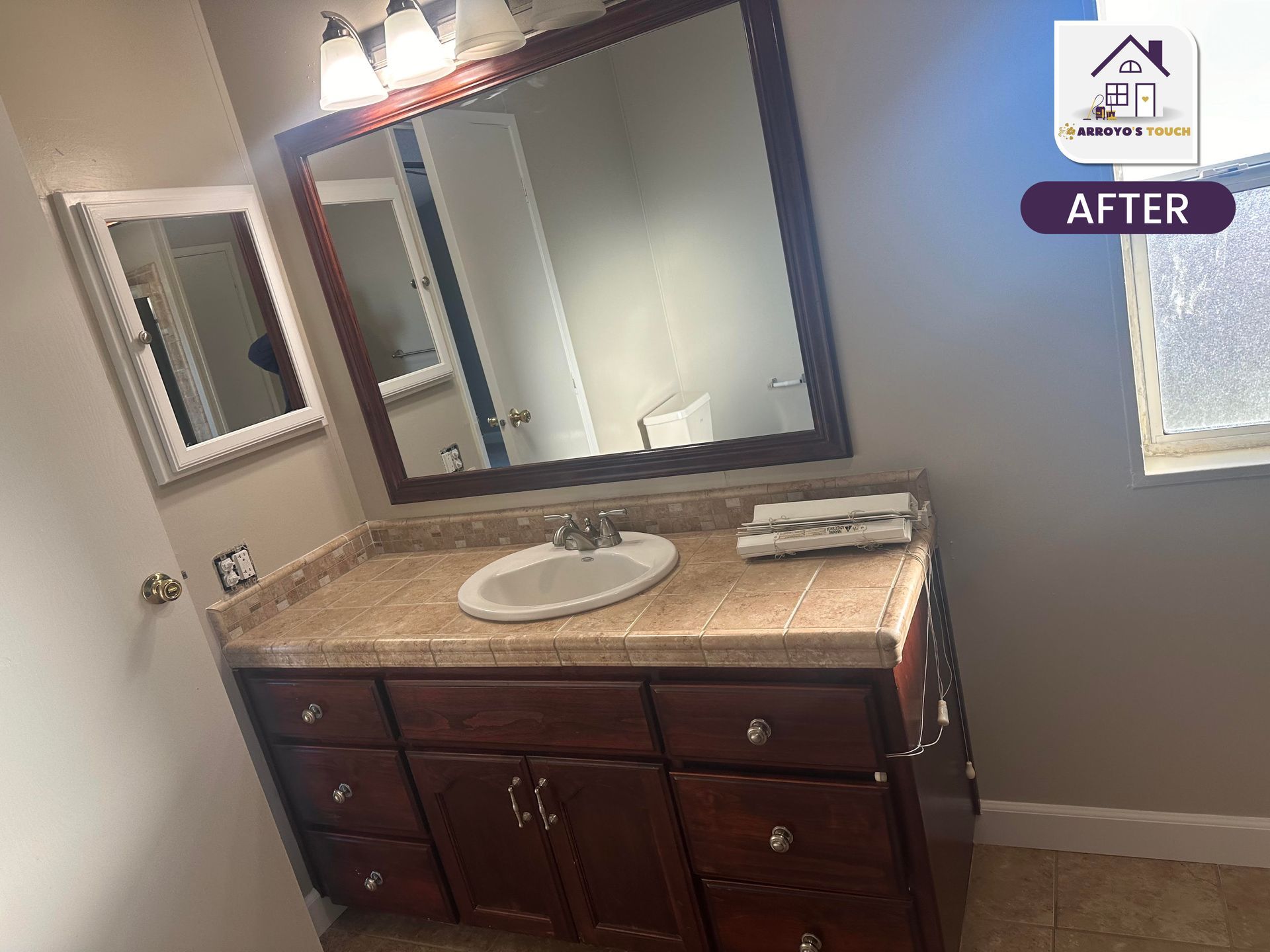 Bathroom with dark wood vanity, light countertop, large mirror, and small window.