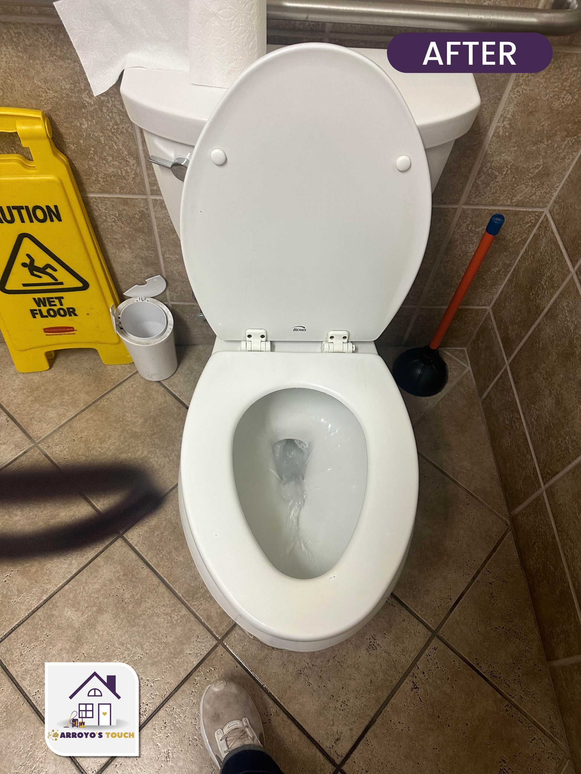 White toilet in a tiled bathroom with the seat up. A wet floor sign and plunger are visible.