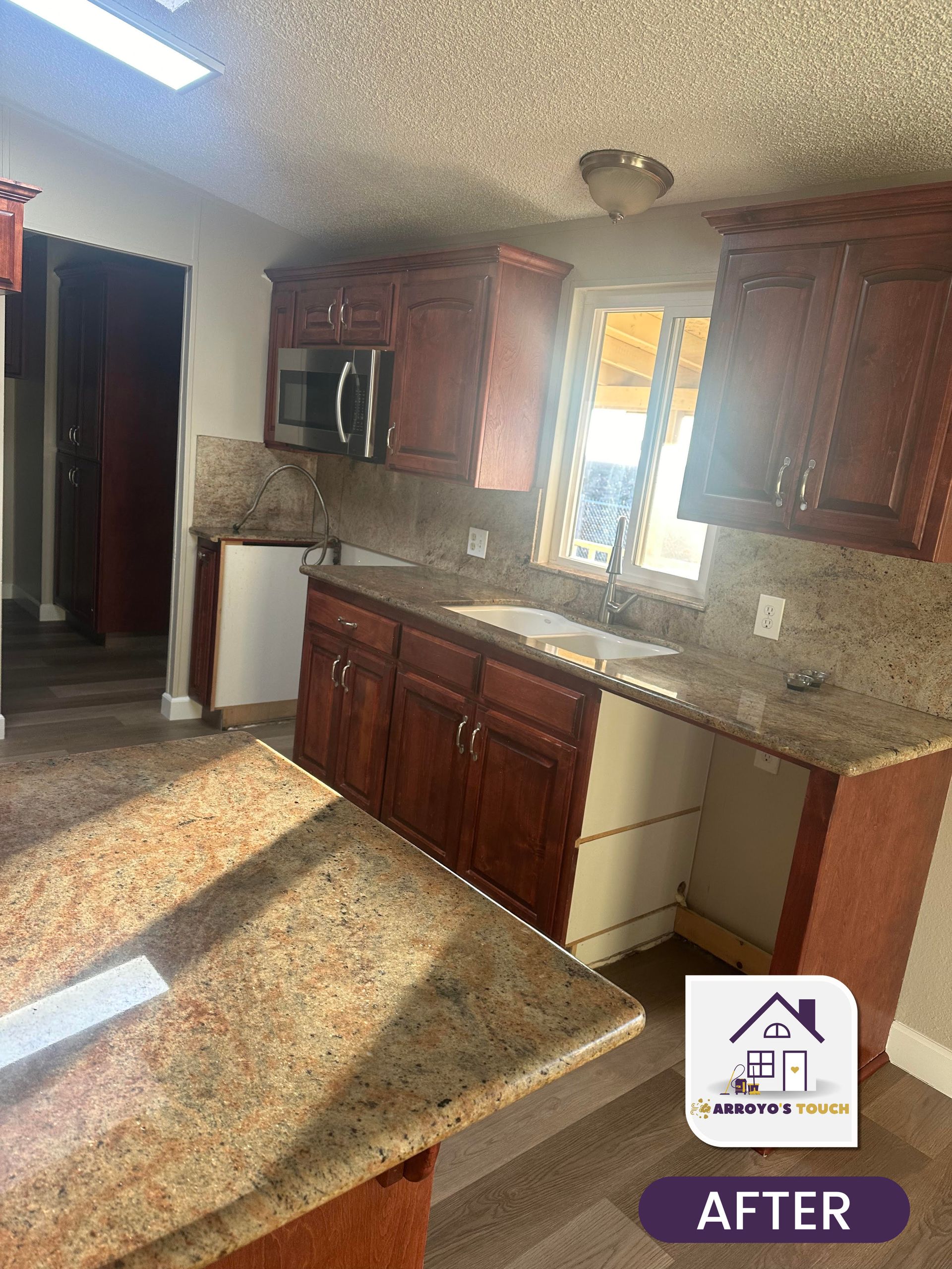 Newly remodeled kitchen with granite countertops and cherry-colored cabinets. Sunlight streams through a window.
