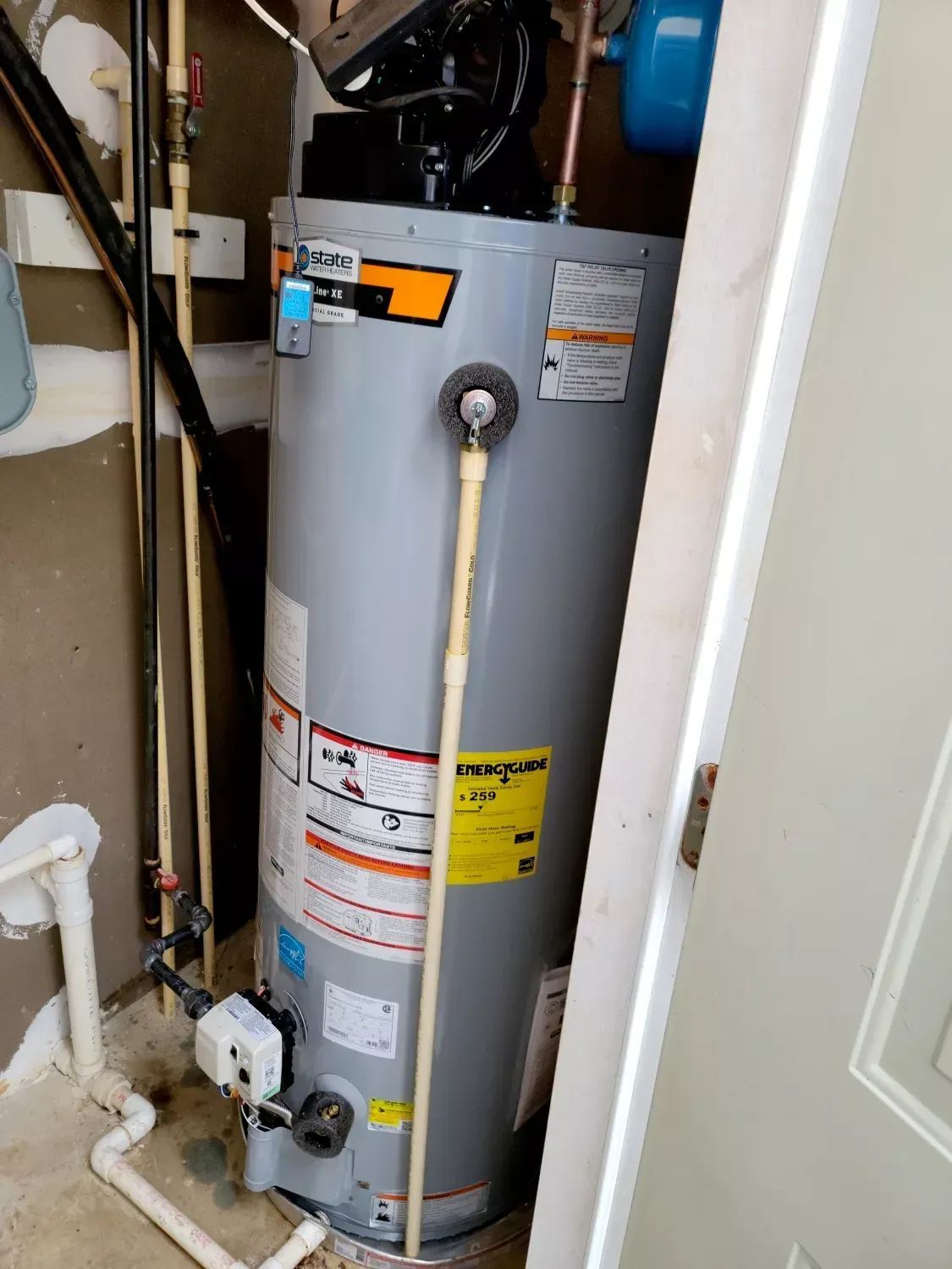 Water heater in a narrow utility closet with exposed pipes and labels.