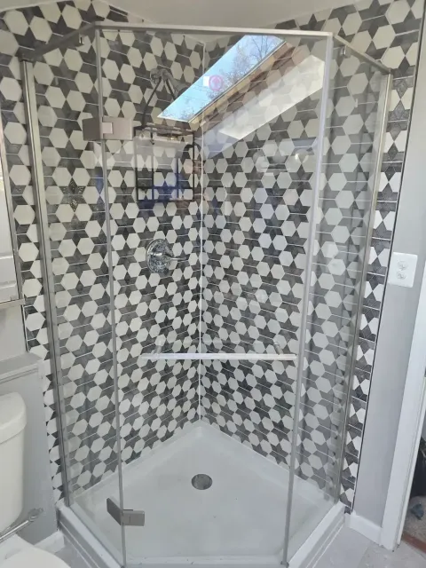 A bathroom with a walk in shower with a black and white tile wall.