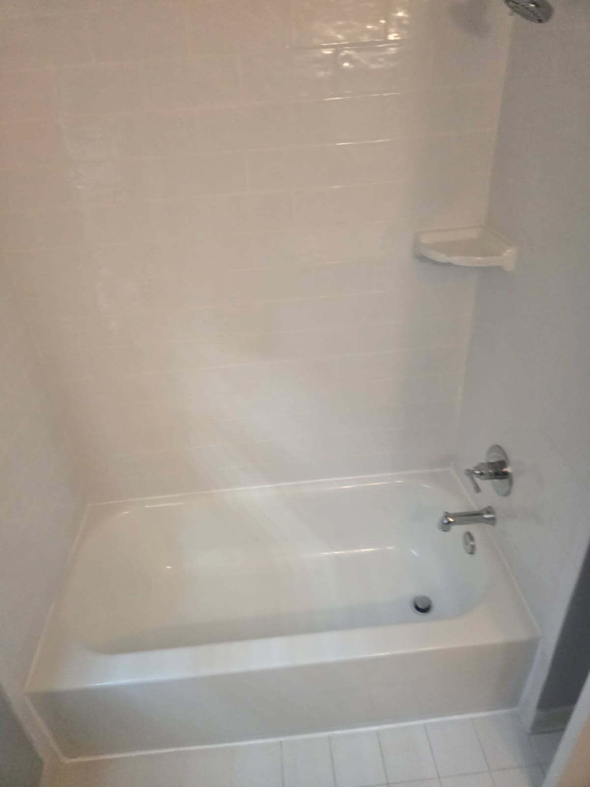 Empty white bathtub and shower in a tiled bathroom, with a chrome faucet and built-in soap shelf.