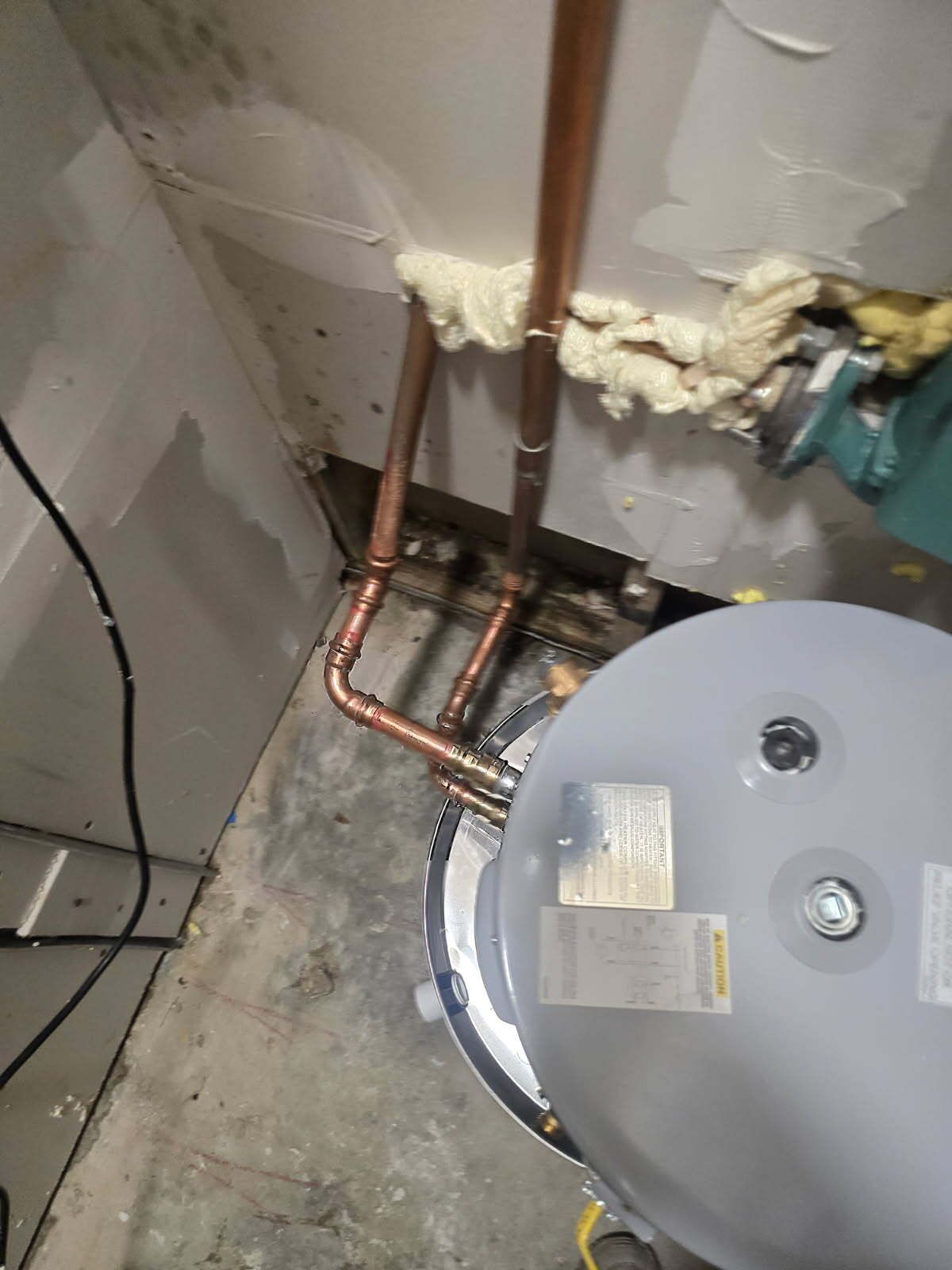 Copper pipes and a water heater in a basement corner with unfinished concrete floor and wall insulation foam.