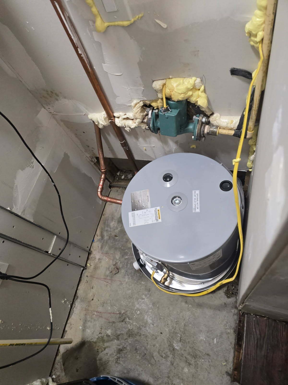 Utility room with a round water heater tank beside exposed pipes and a concrete floor