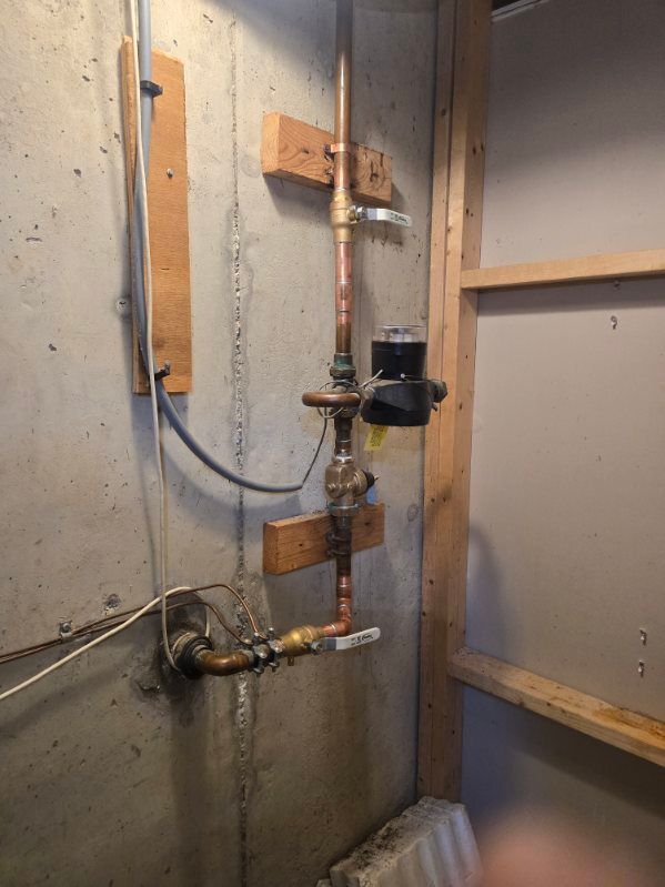 Utility pipes and a water meter on a bare concrete basement wall.