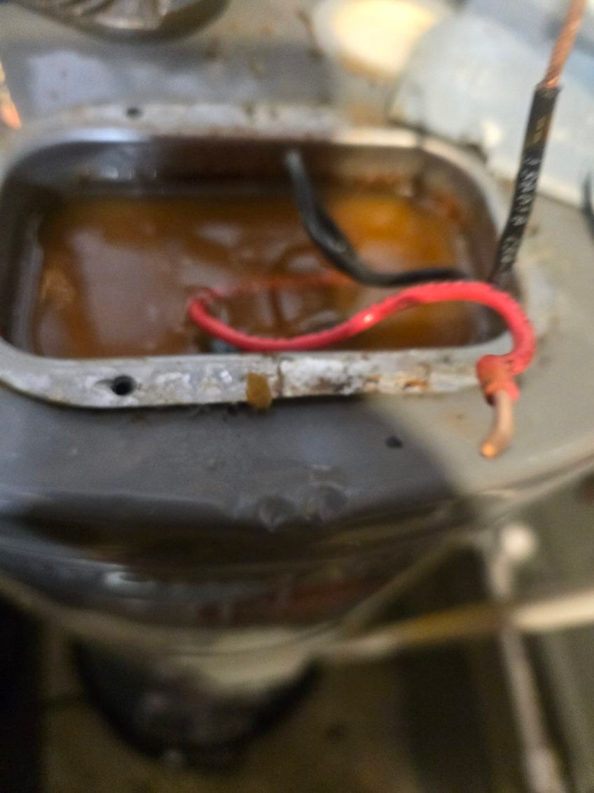 Close-up of a rusty metal container with brown liquid and red and black wires inside.