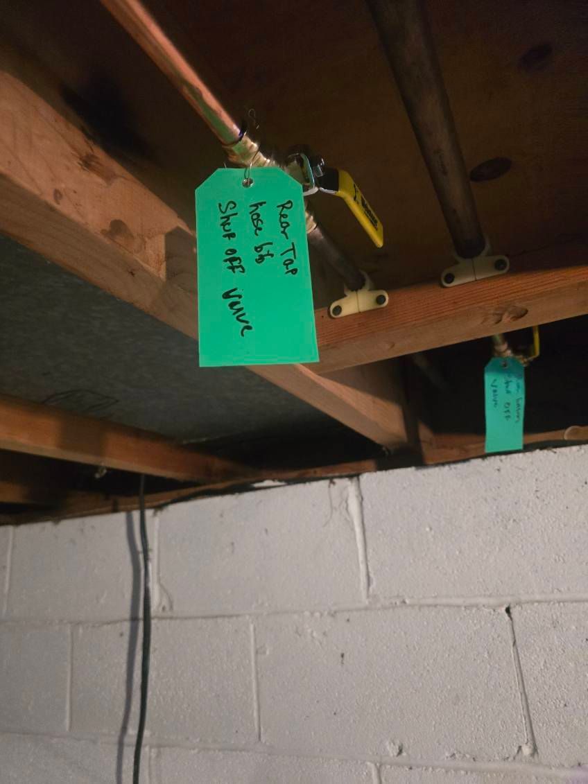 Tags hanging from pipes under a basement ceiling above a cinderblock wall.