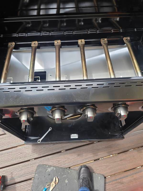 Close-up of a stainless steel gas grill with five burners and control knobs on a wooden deck.