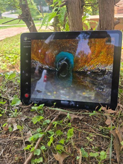 Tablet propped on grass showing a motorcycle riding through water in an autumn scene