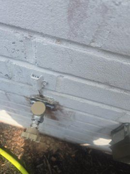 White exterior wall with a utility meter, pipes, and a small stain near the ground.