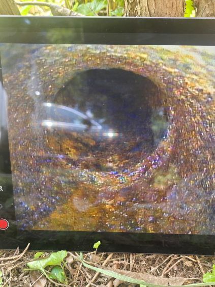 Close-up of a dark circular hole in a rusted metal surface with reflective glare.