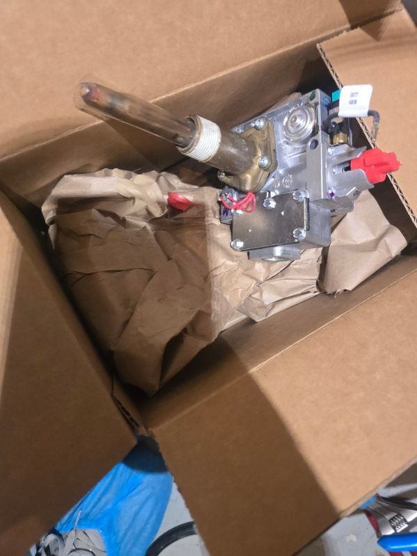 Metal valve assembly and glass tube in a cardboard box with packing paper and blue gloves nearby