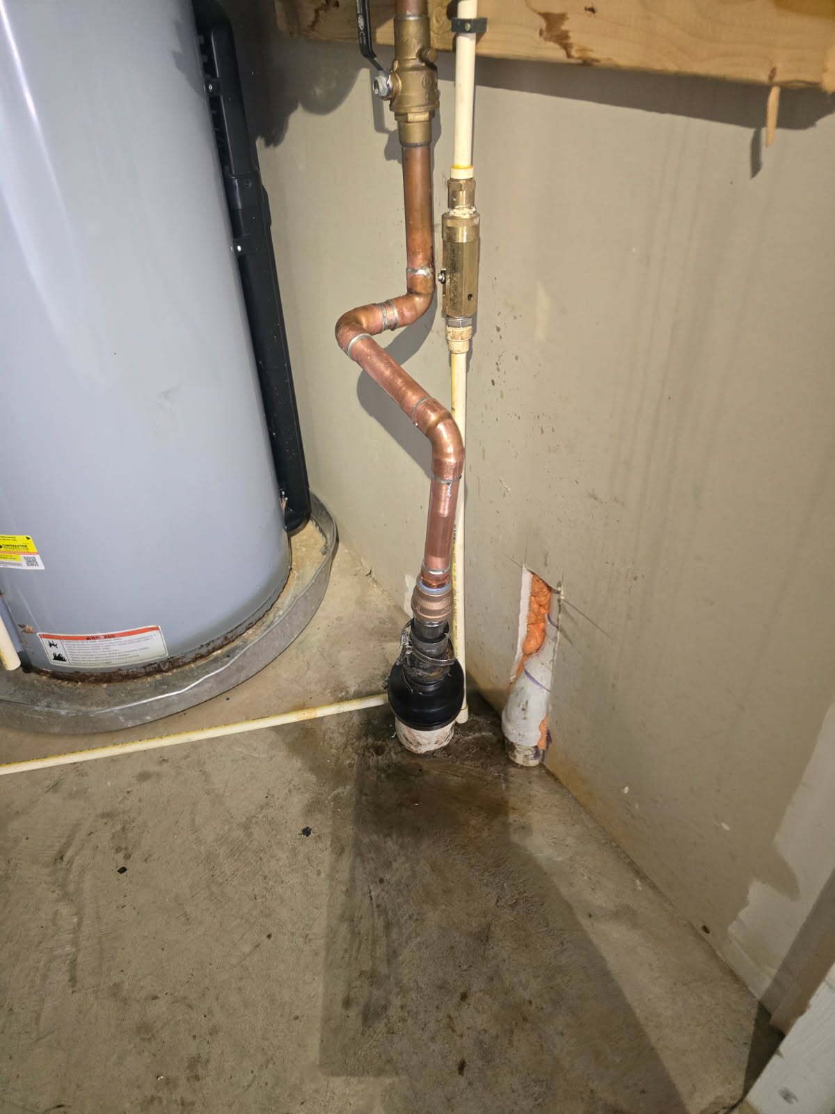 Copper plumbing pipe beside a water heater in a utility corner with a wet concrete floor.