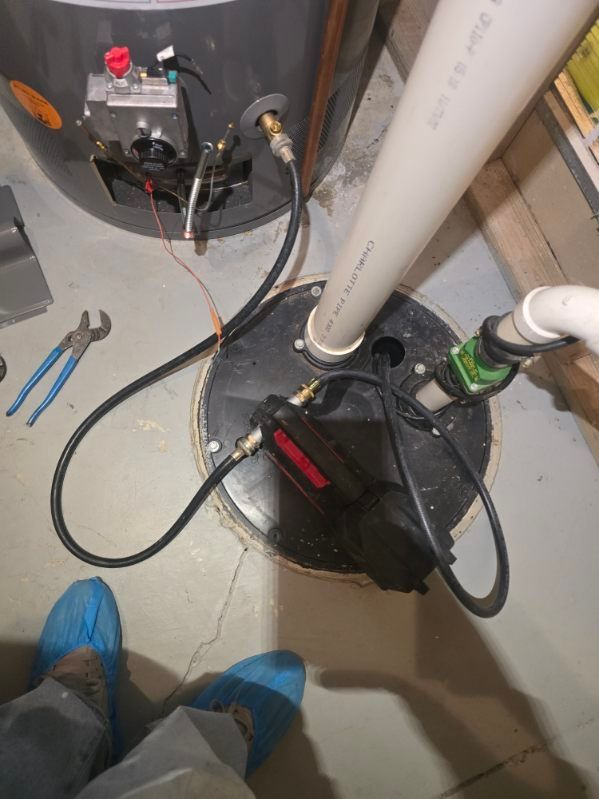 Basement utility area with water heaters, pipes, tools on the floor, and blue shoe covers visible.