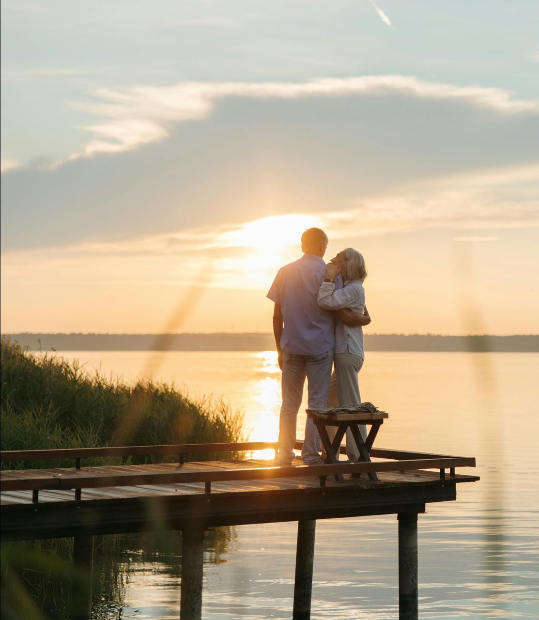 Couple embracing on a dock, watching a sunset over a calm lake.