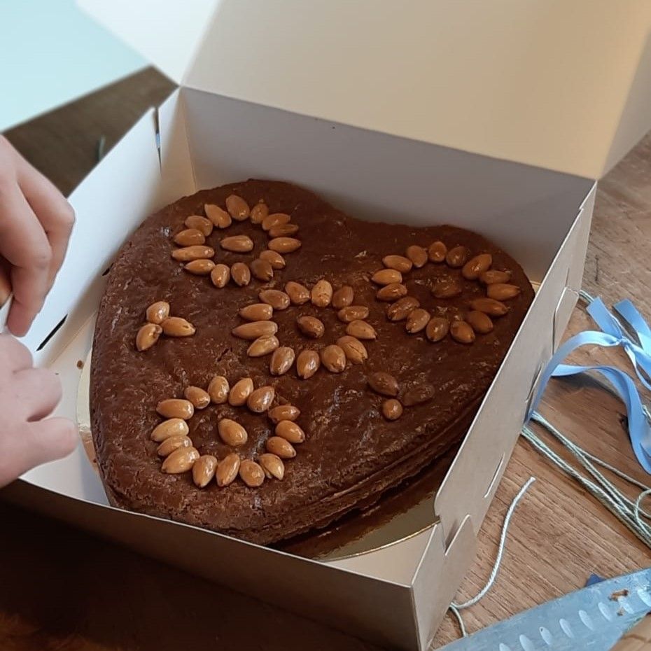 Hartvormige taart in een doos, versierd met noten in bloemmotieven. Een kinderhandje reikt erin.