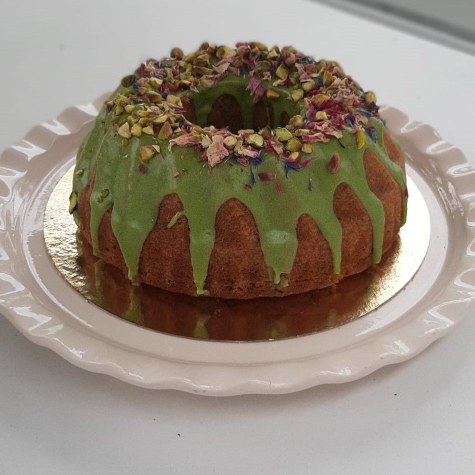 Een tulbandcake met groene glazuur en pistachetopping op een roze bord.