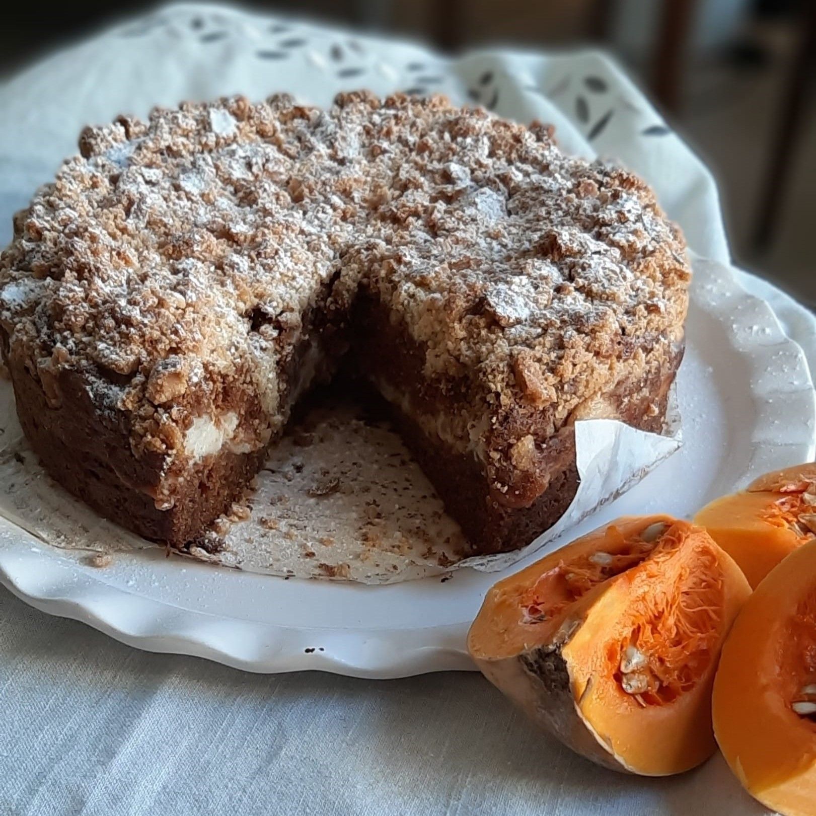 Taart met kruimeltopping, in plakjes gesneden zodat de vulling zichtbaar is, op een bord met plakjes pompoen.