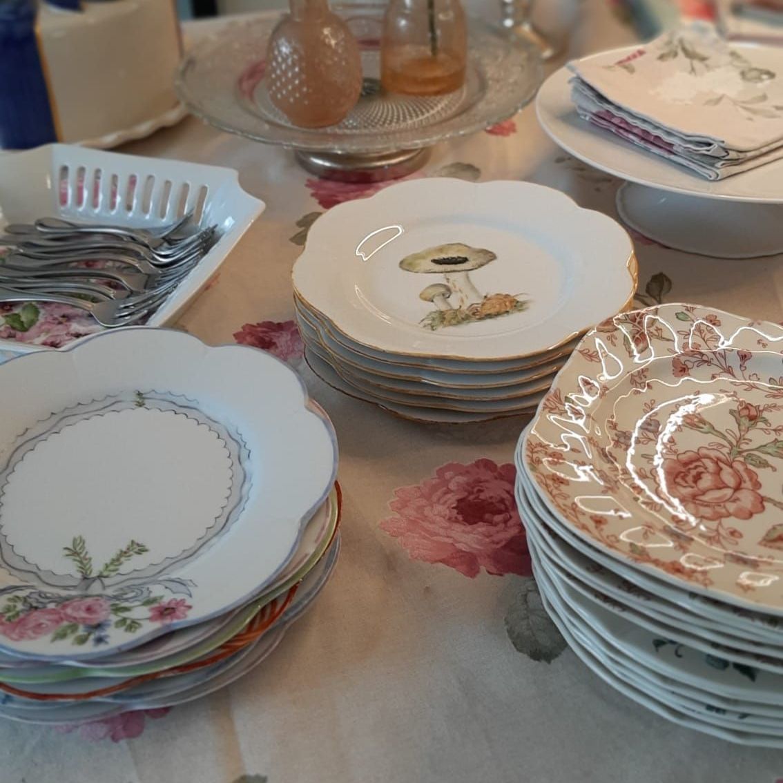 Close-up van diverse vintage borden opgestapeld op een bloemenkleed. Sommige hebben gouden randen en unieke versieringen.