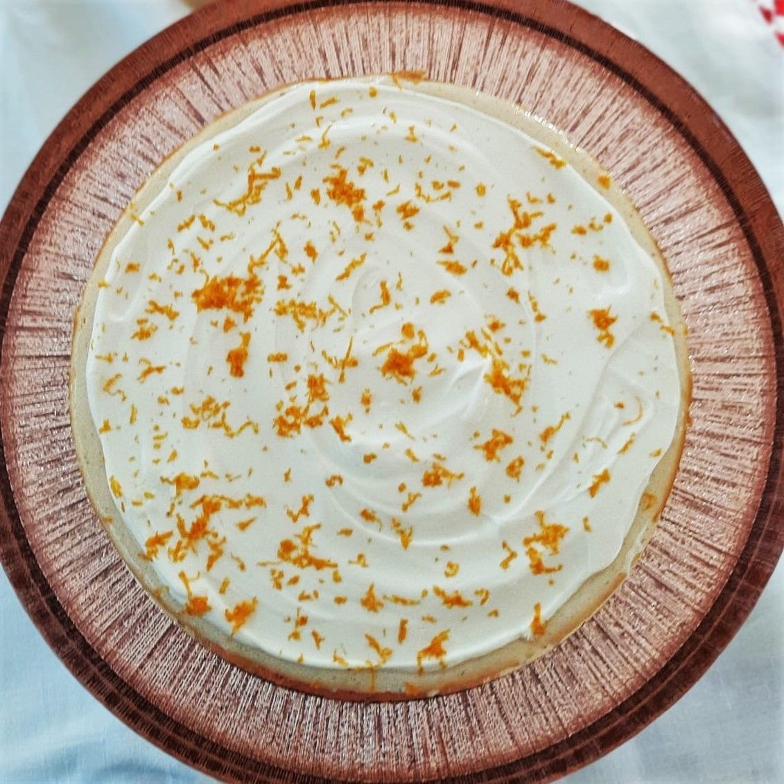 Taart met witte glazuur en sinaasappelschil op een houten bord.
