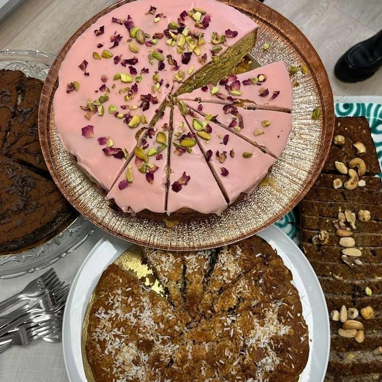 Taarten op tafel: een ronde taart met roze glazuur, in plakken gesneden; andere taarten met diverse toppings, bestek.