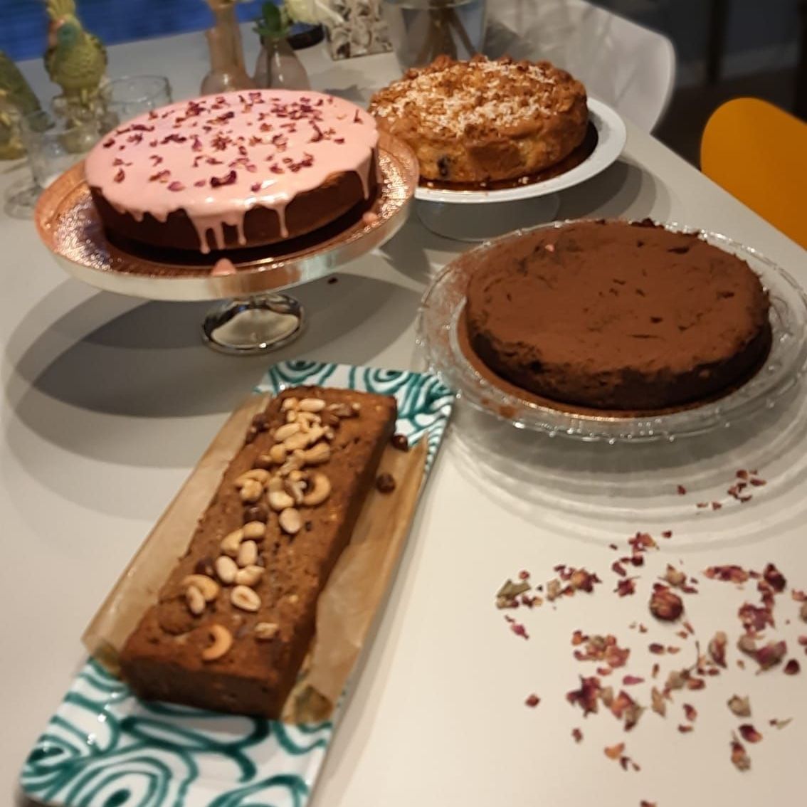 Taarten en een brood op tafel: een roze geglazuurde taart, appeltaart, chocoladetaart en een brood met noten.