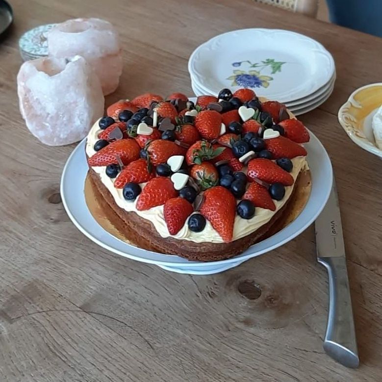 Hartvormige taart met aardbeien, bosbessen en chocolade, op een wit bord op een houten tafel.