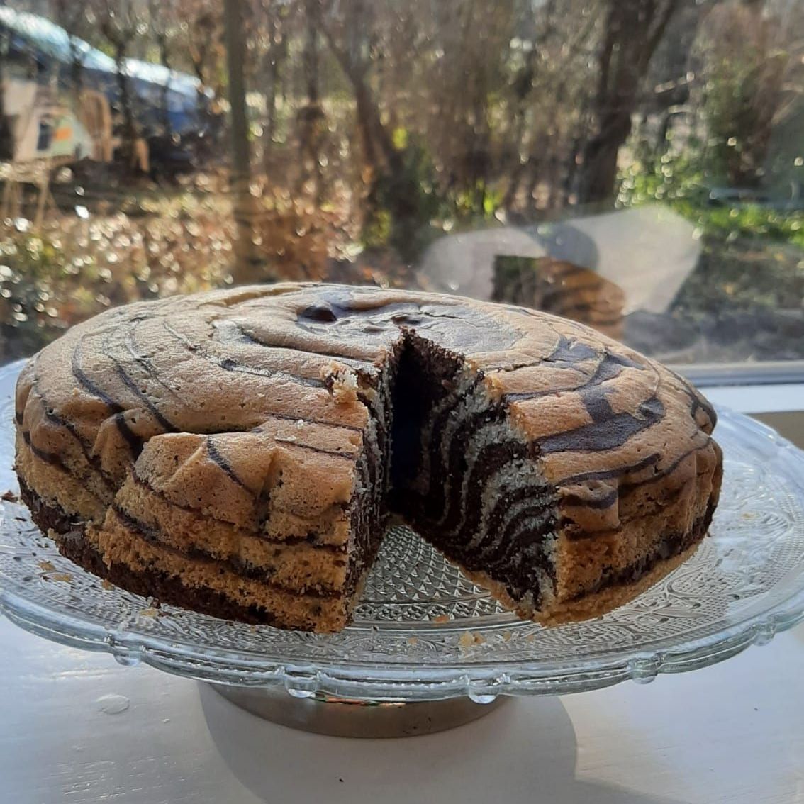 Zebra-gestreepte taart op een glazen serveerschaal, met een afgesneden stuk. Bruine en beige tinten, natuurlijk licht.
