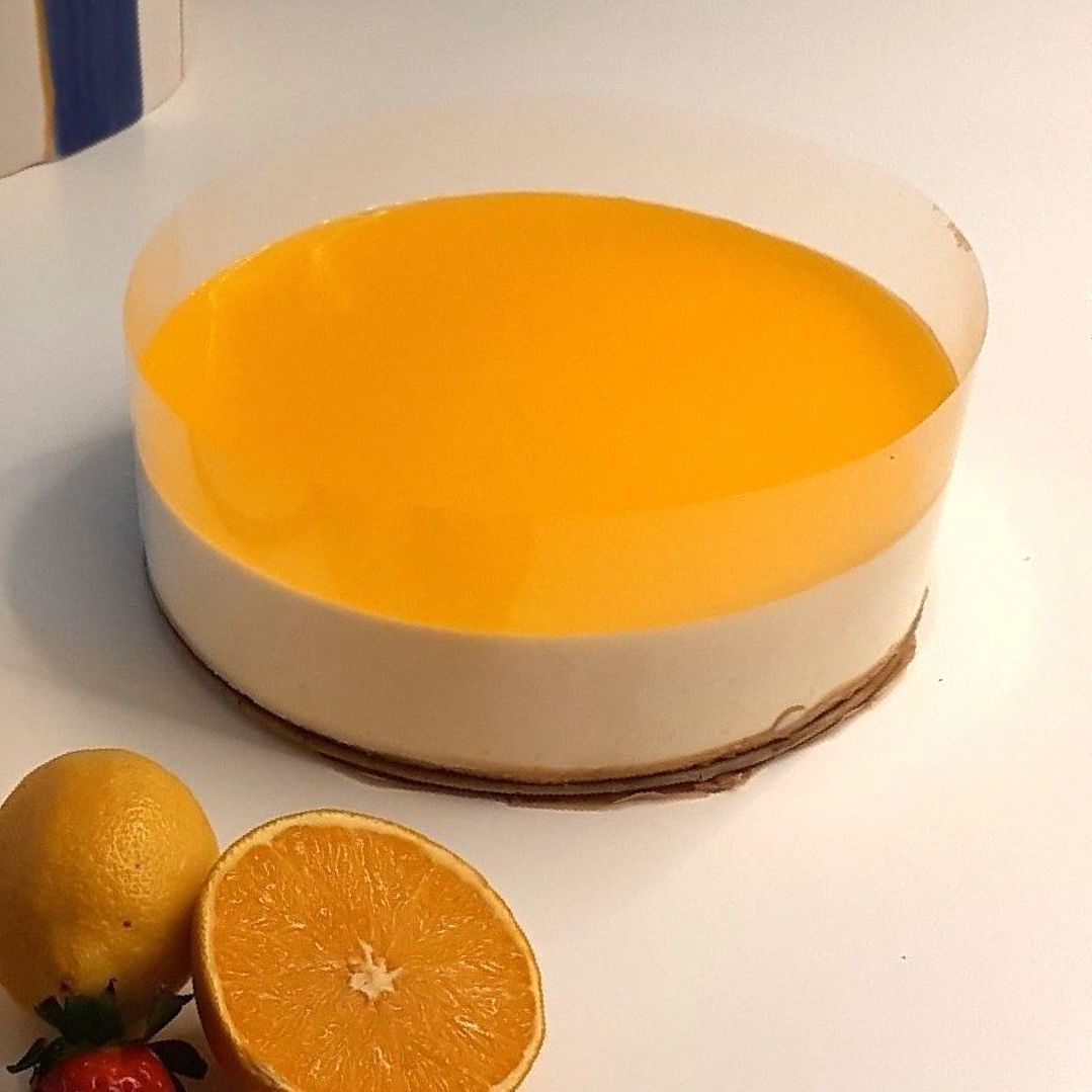 Citroen-sinaasappelcheesecake met gele glazuur, geserveerd met een schijfje citroen, een schijfje sinaasappel en een aardbei.