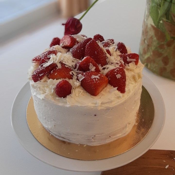 Taart met witte glazuur, gegarneerd met aardbeien en witte chocoladeschaafsel, op een bord.