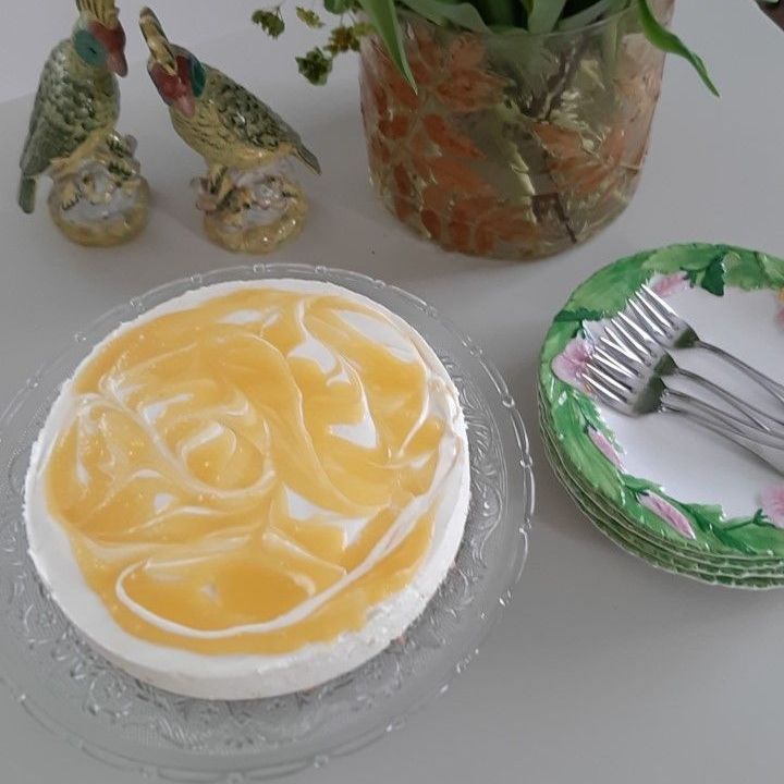Cheesecake met gele swirl topping, naast bordjes en vogelfiguurtjes.