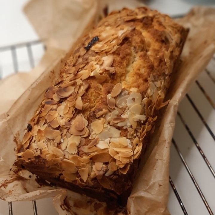 Cake in cakevorm met amandeltopping, gewikkeld in bakpapier en afgekoeld op een rooster.