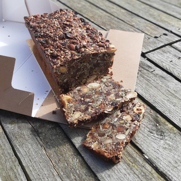 Een brood met zaden, gedeeltelijk in plakjes gesneden, in een kartonnen doos op een houten ondergrond.