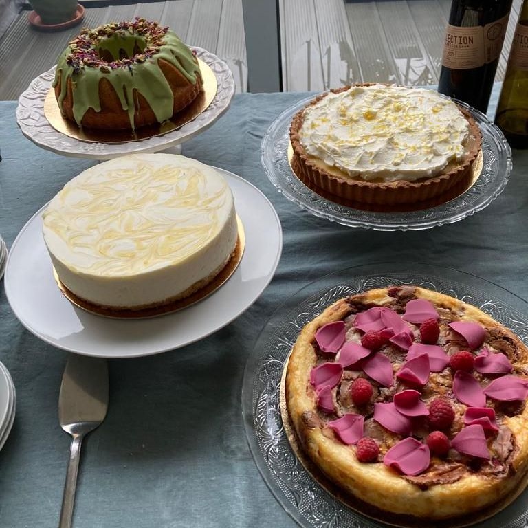 Taarten uitgestald op een tafel. Onder andere een tulbandcake, cheesecake, taart en cheesecake met frambozen.