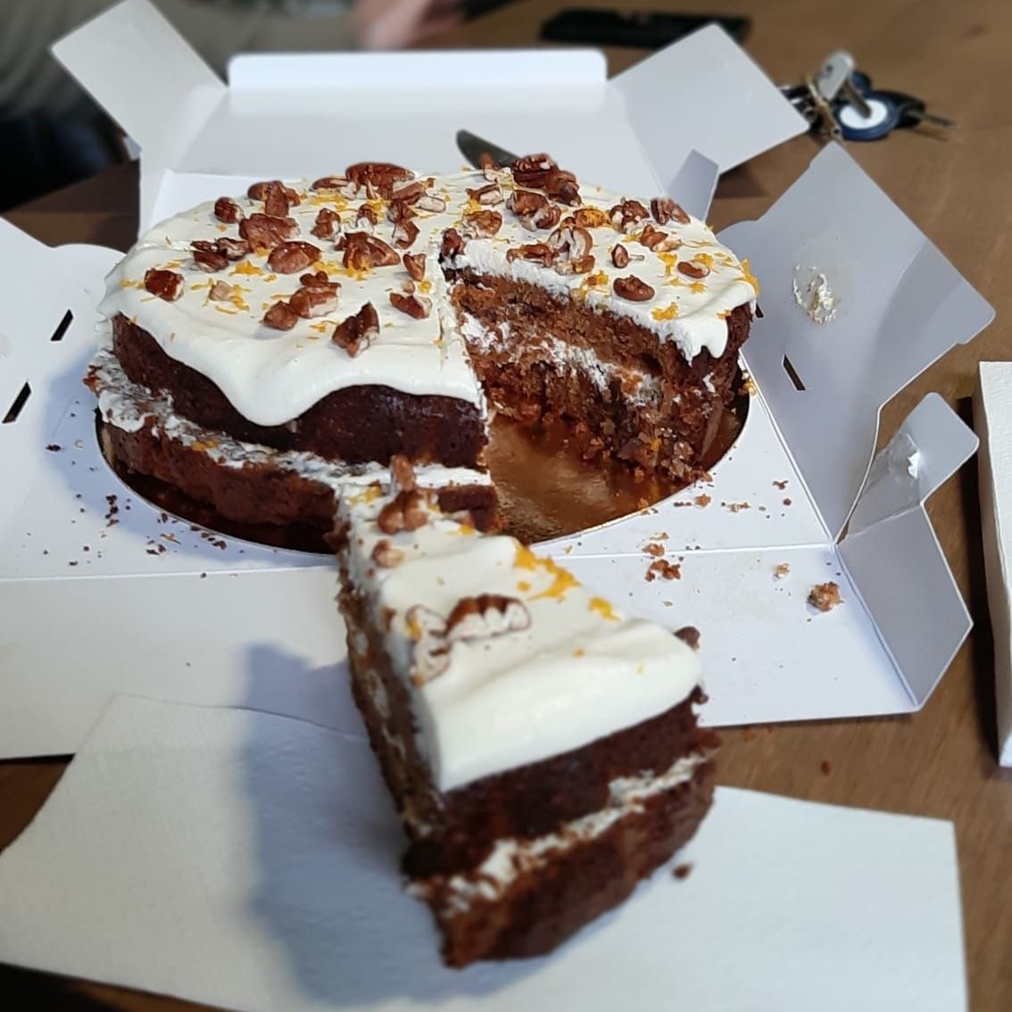 Worteltaart met witte glazuur en pecannoten, in plakjes gesneden in een witte doos.