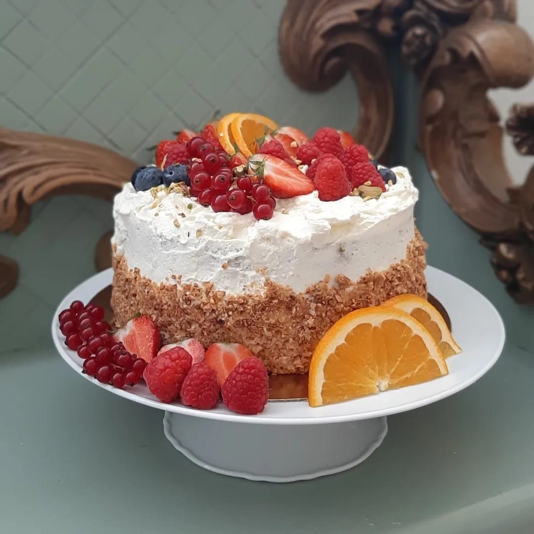 Taart op een witte sokkel met slagroom, bessen en sinaasappelschijfjes.
