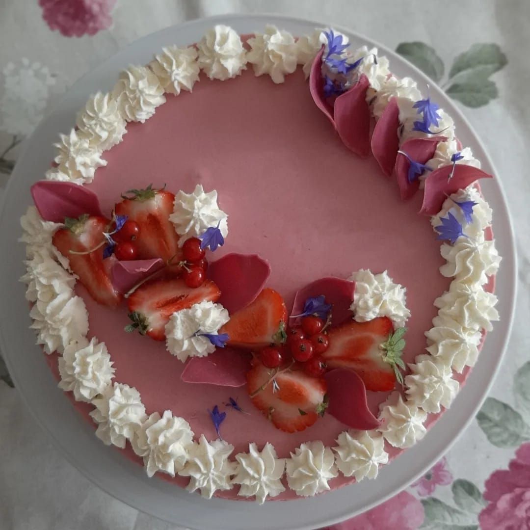 Roze taart met glazuur, een witte crèmerand, aardbeien, rode bessen en paarse bloemblaadjes.