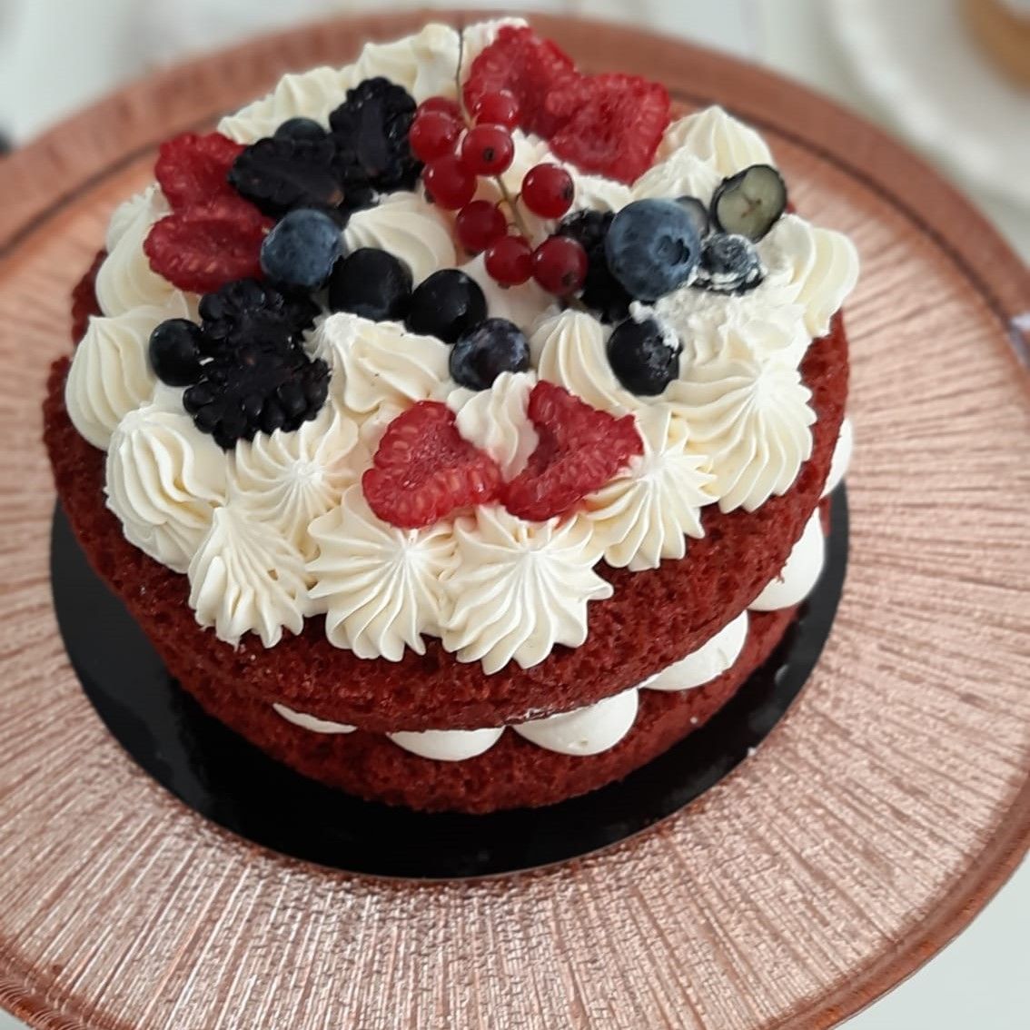 Rode fluwelen cake met witte glazuur en bessen op een roségouden bord.