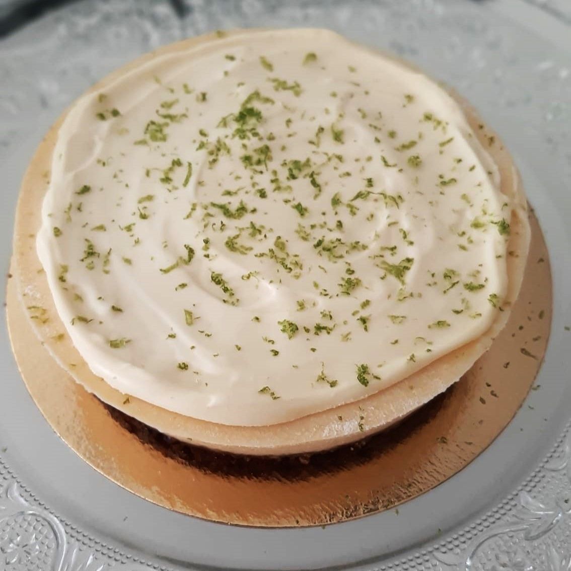 Klein rond cakeje met witte glazuur en groene citroenschil erop.