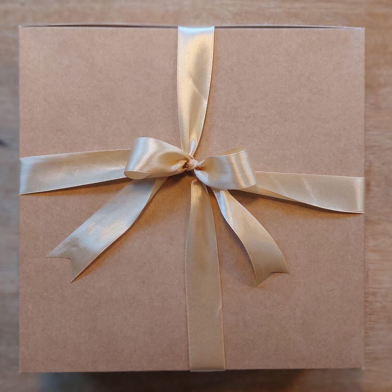 Een kartonnen geschenkdoos, vastgebonden met een gouden satijnen lint, op een houten ondergrond.