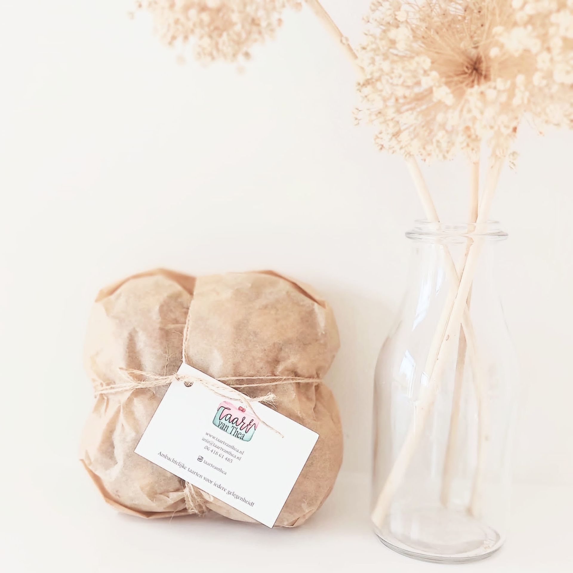 Een in bruin papier verpakt pakketje met label, vastgebonden met touw, naast een doorzichtige vaas met gedroogde bloemen.
