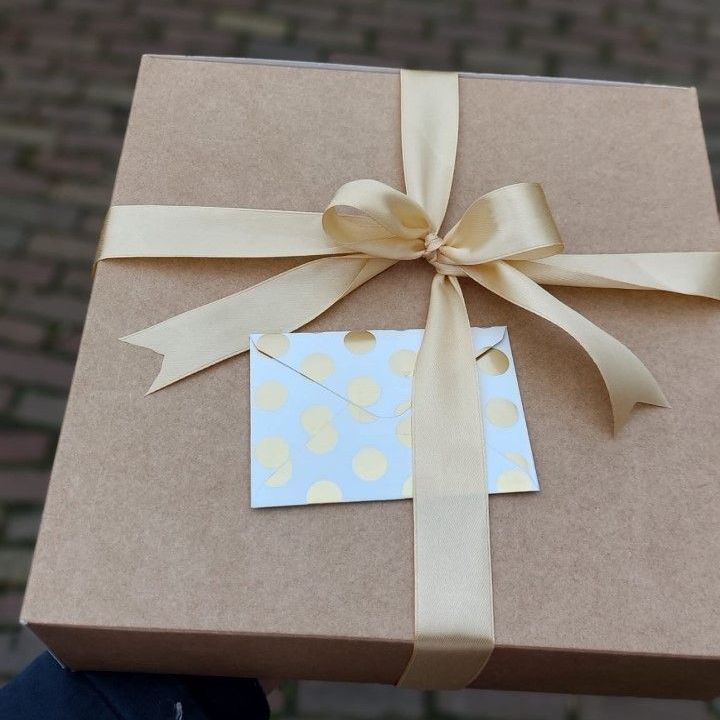Bruine vierkante geschenkdoos, vastgebonden met een gouden lint en strik, met een klein kaartje met gouden stippen.
