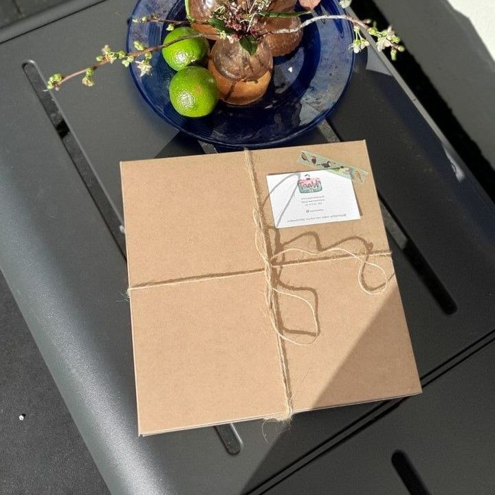 Een bruin pakket, vastgebonden met touw, ligt op een grijze tafel, met een limoen en een bord met eten op de achtergrond.
